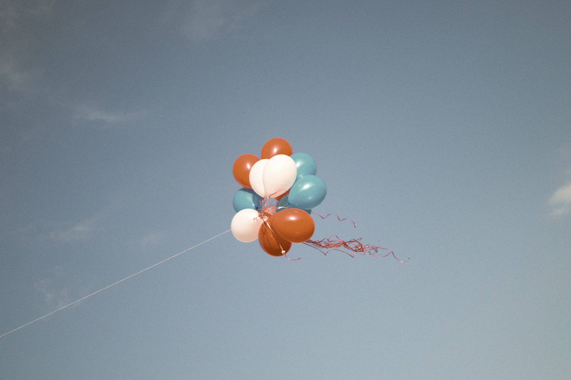 Cluster of colorful balloons floating against a clear blue sky. Vibrant and uplifting.