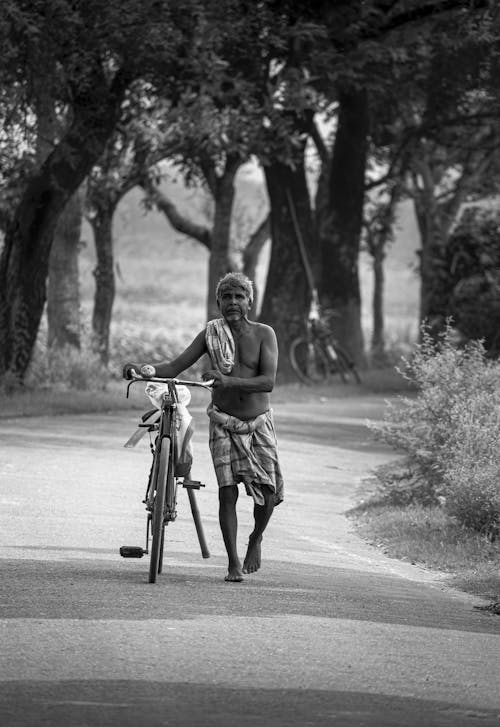 Black and White Photo of a Shirtless Man Walking with His Bicycle