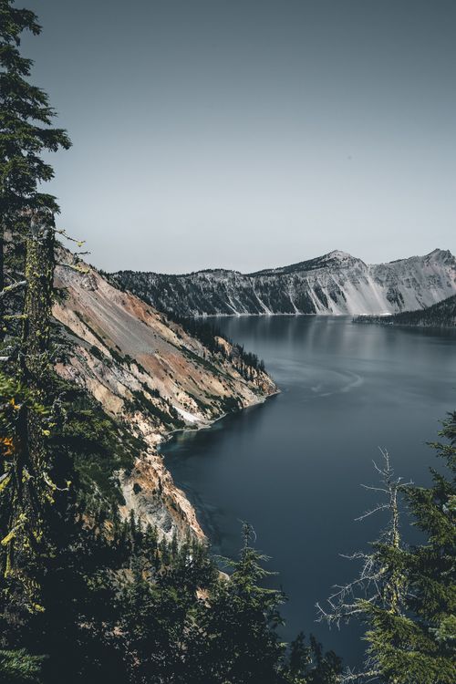 Free Breathtaking view of Crater Lake's clear waters surrounded by rugged mountains and lush trees. Stock Photo