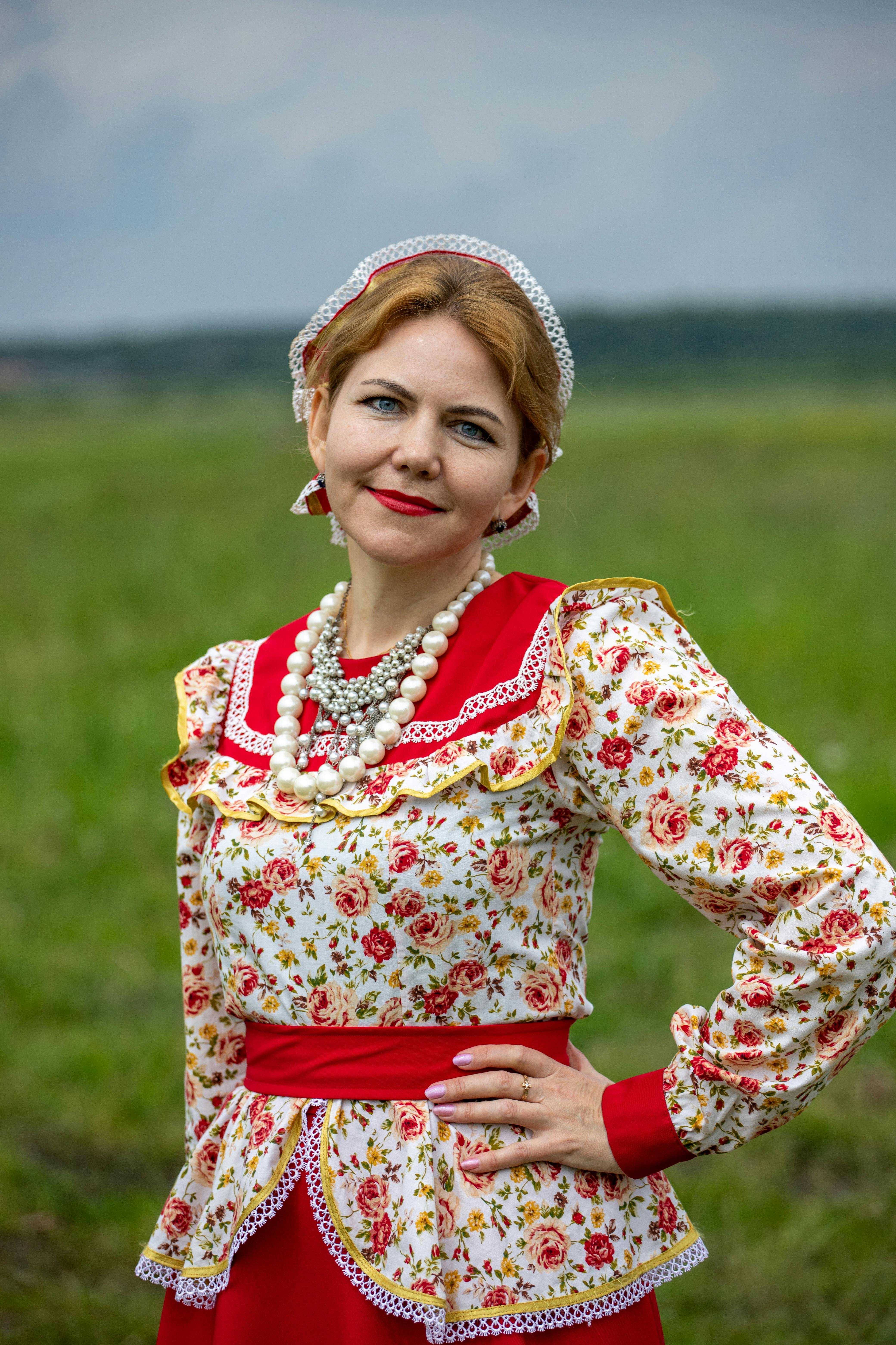Caucasian woman in floral dress posing outdoors with a cheerful smile.