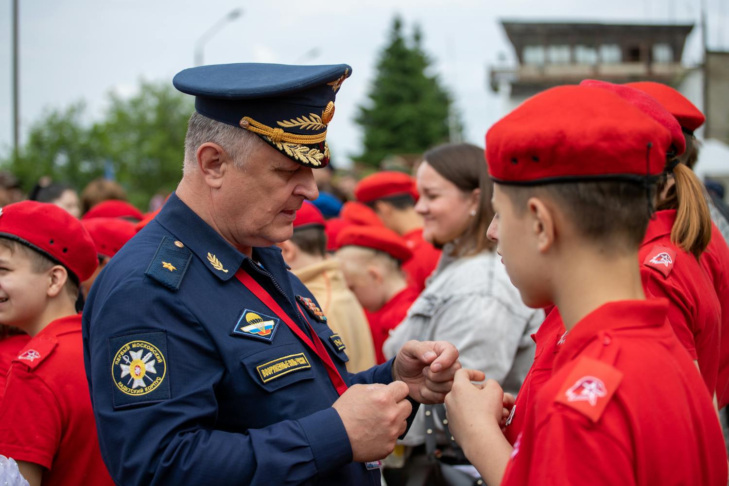 A military officer engages with youth cadets in uniform at an outdoor event.