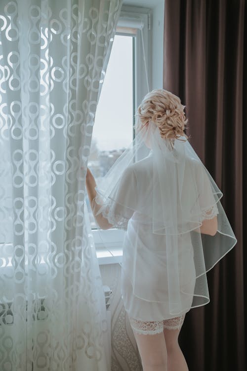 Woman in White Wedding Dress Standing Near the Window