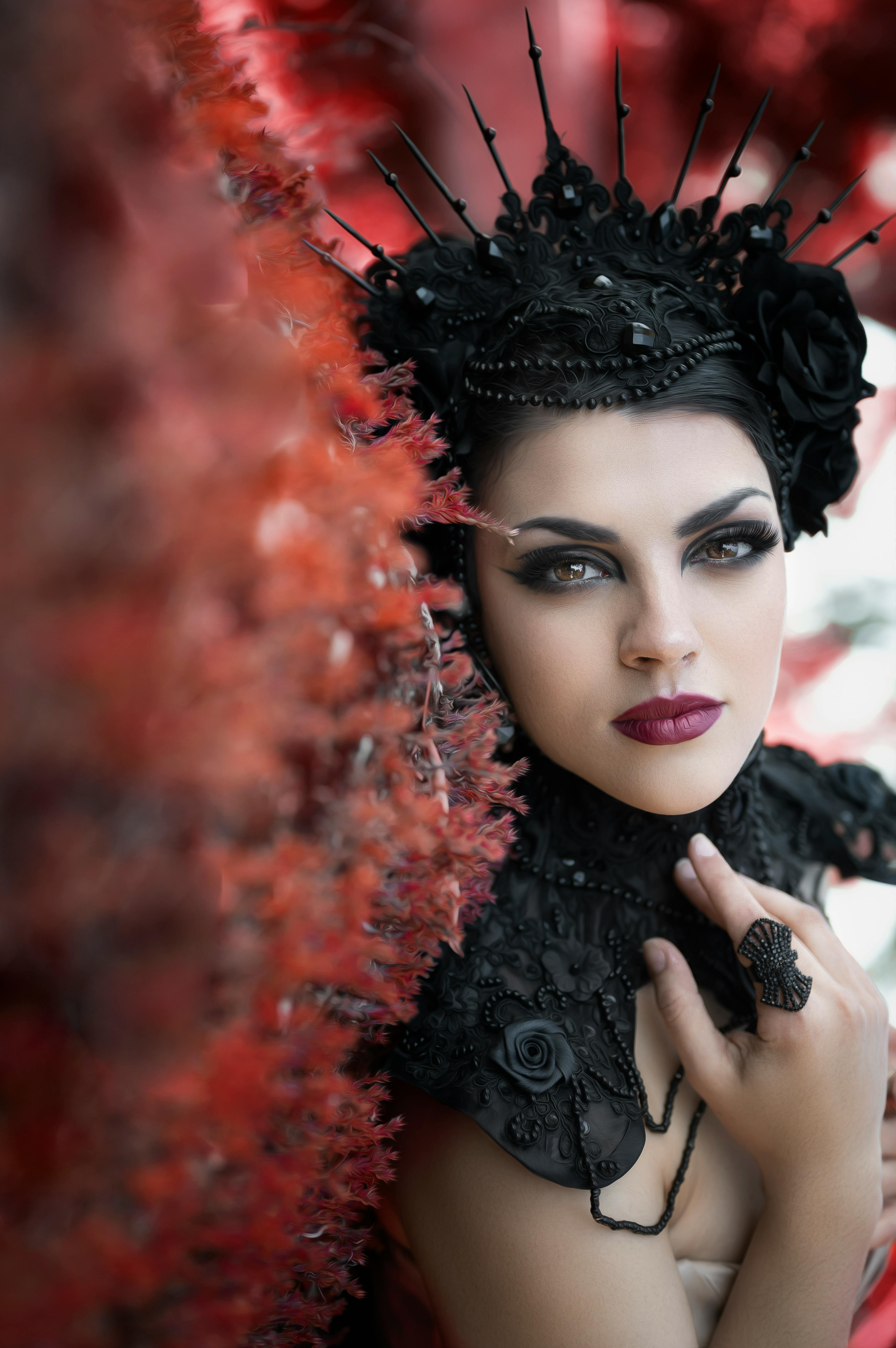 Striking portrait of a woman in a detailed black headdress with vibrant red background.