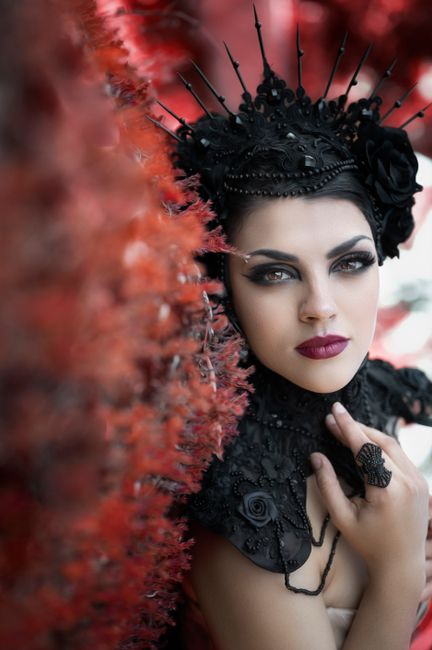 Striking portrait of a woman in a detailed black headdress with vibrant red background.