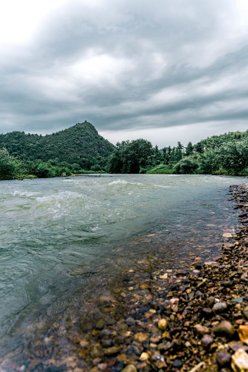 Free A picturesque mountain landscape with a flowing river under a gloomy sky, showcasing nature's beauty. Stock Photo