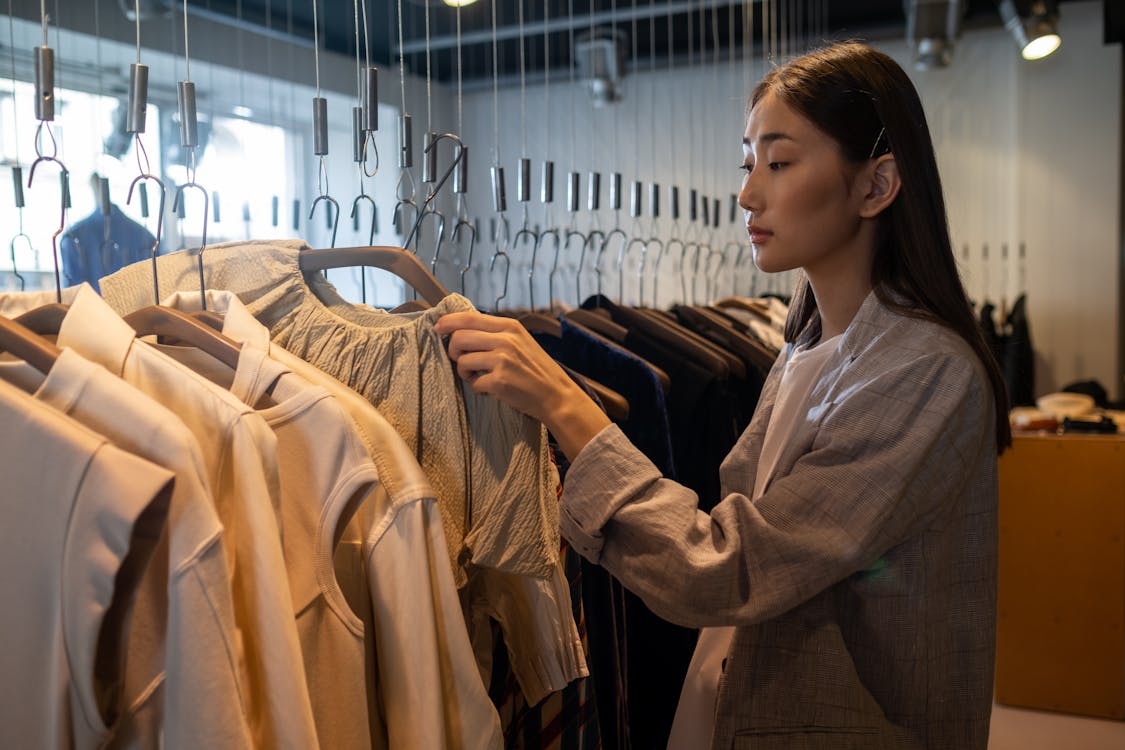 Woman in Gray Coat Holding Clothes Hanger With Clothes - Thrift Stores