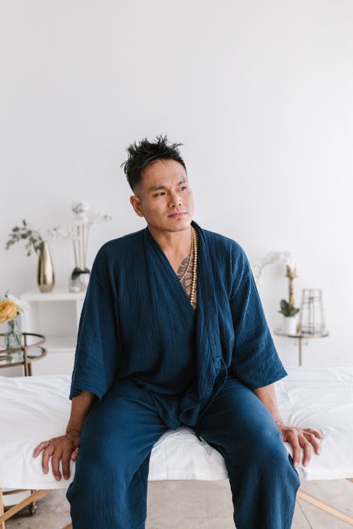 Free A man in a blue robe reflects while sitting on a bed in a serene indoor setting. Stock Photo