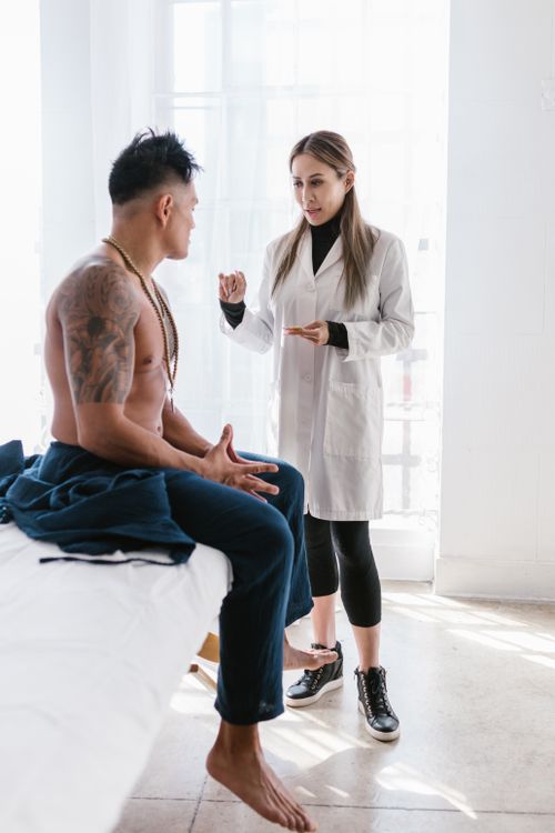 Free Female doctor consults with tattooed male patient indoors in bright room. Stock Photo