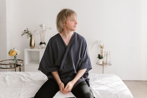 Free Caucasian man in a spa setting wearing a robe, seated on a bed, embracing tranquility. Stock Photo