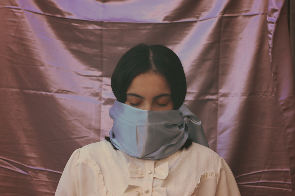 Woman draped in a blue silk scarf against a fabric background