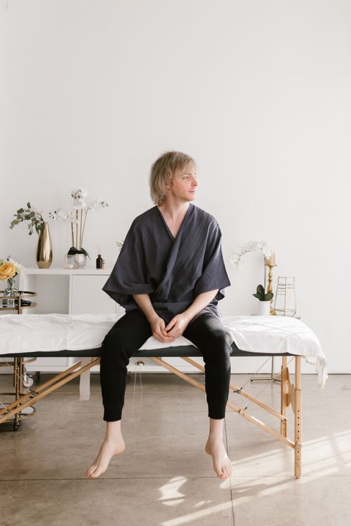 Free Caucasian man in spa setting, sitting relaxed on a massage table in a minimalist room, suggesting wellness and tranquility. Stock Photo
