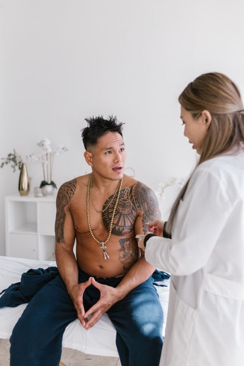 Free A shirtless man with tattoos discusses health with a female doctor indoors. Stock Photo