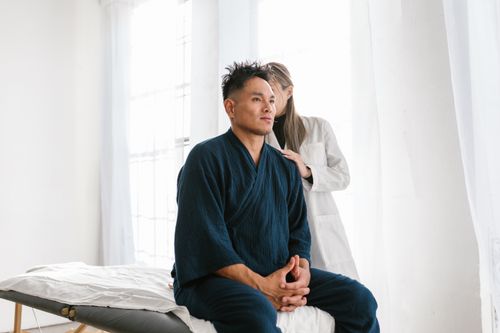 Free A doctor examines a patient seated on a treatment table in a medical facility. Stock Photo