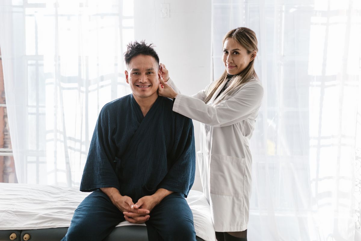 A doctor in a white coat examines a smiling patient indoors in a bright setting
