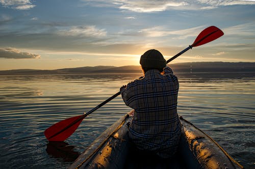 A Back View of a Person in Plaid Long Sleeves Sitting on the Boat while Paddling
