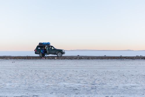 Free A 4x4 SUV with travelers in the vast, icy landscape of the Salar de Uyuni at sunrise. Stock Photo