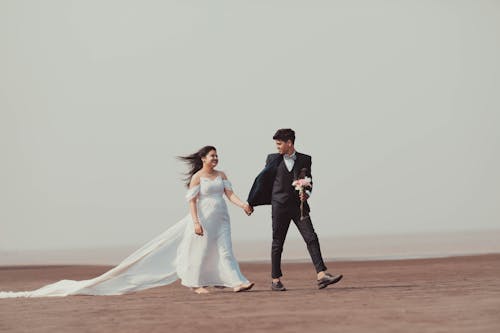 A Newlywed Couple Holding Hands while Walking