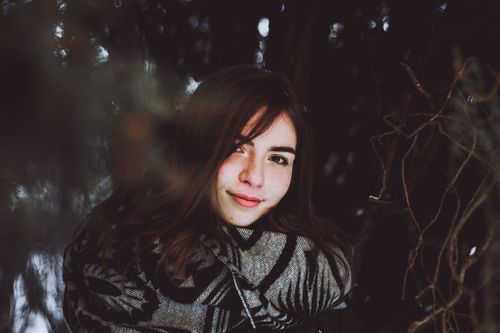 Free A beautiful young woman wrapped in a cozy scarf smiles softly outdoors in winter. Stock Photo