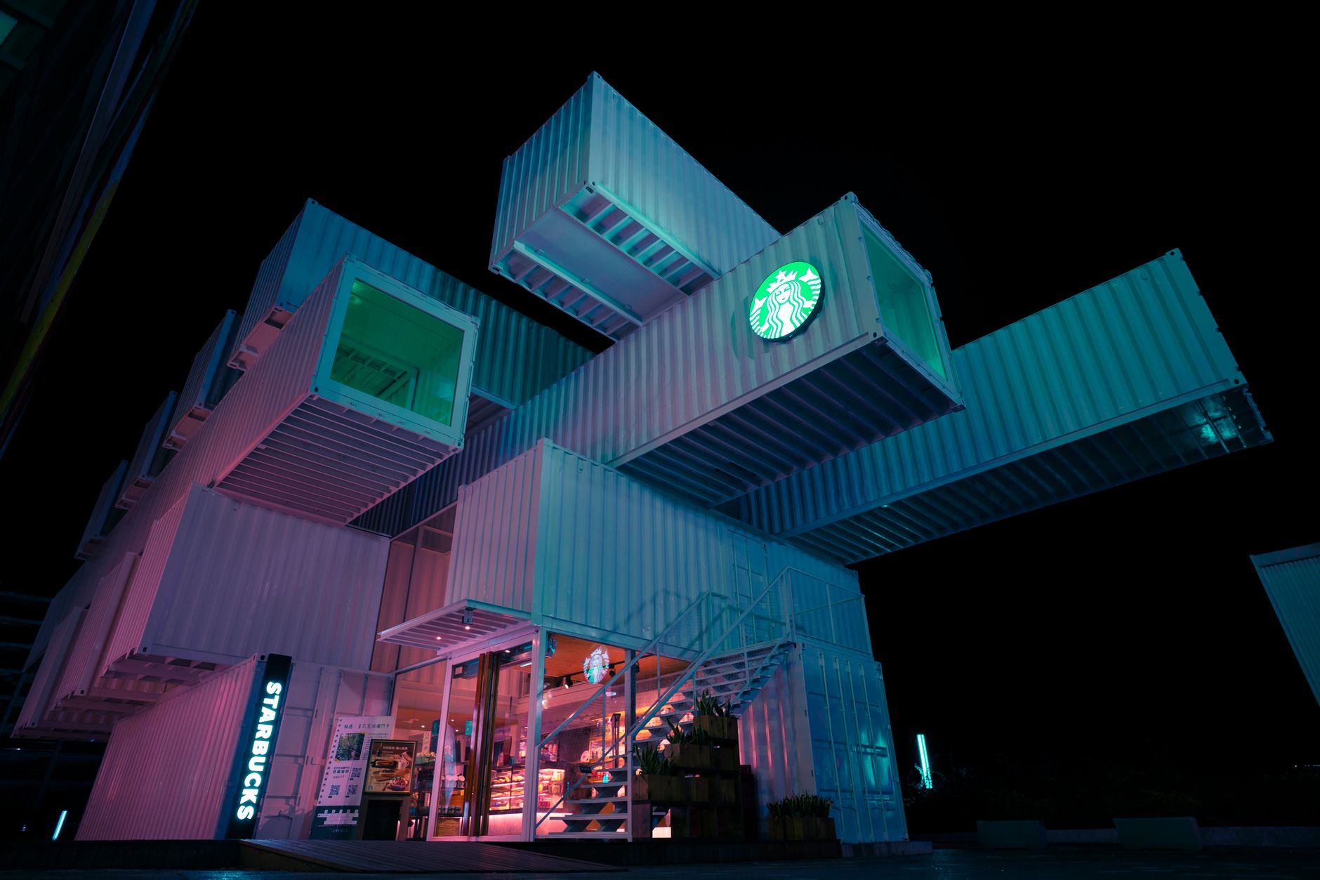 A striking view of a modern Starbucks built from shipping containers, illuminated at night.