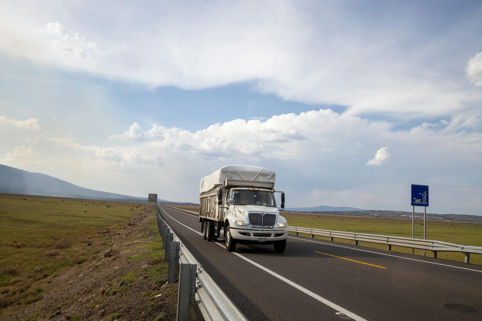 A white truck drives on a scenic highway surrounded by fields in Michoacán, Mexico.