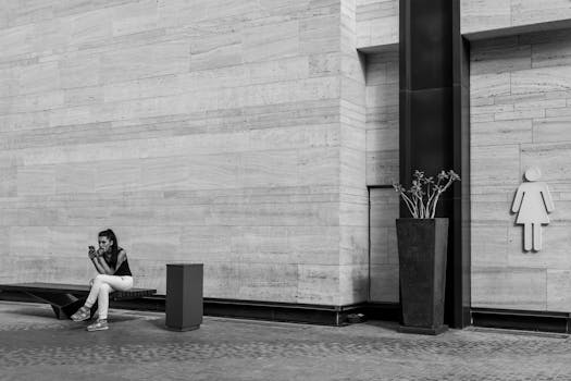 Monochrome shot of a woman using her phone on a bench in a modern urban setting.