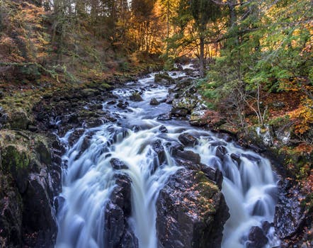Captivating view of a waterfall flowing through an autumn forest in Perthshire, Scotland.