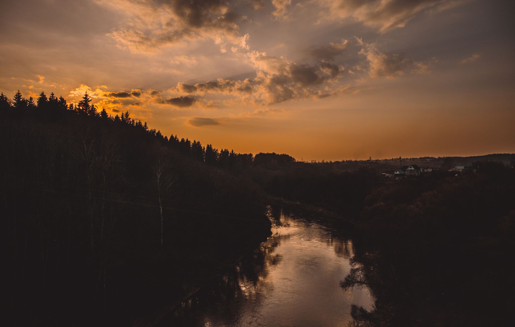 A forested ridge in silhouette above calm canyon water at dusk