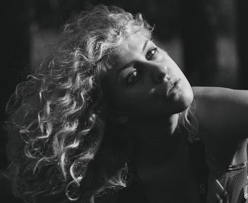 Free Grayscale Photo of a Curly-Haired Woman Looking at Camera while Posing Stock Photo
