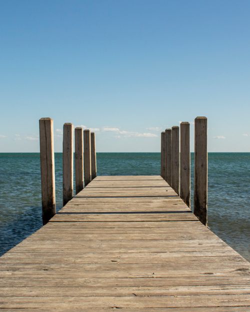 Free A serene view of a wooden pier extending into a calm ocean under a clear blue sky. Stock Photo