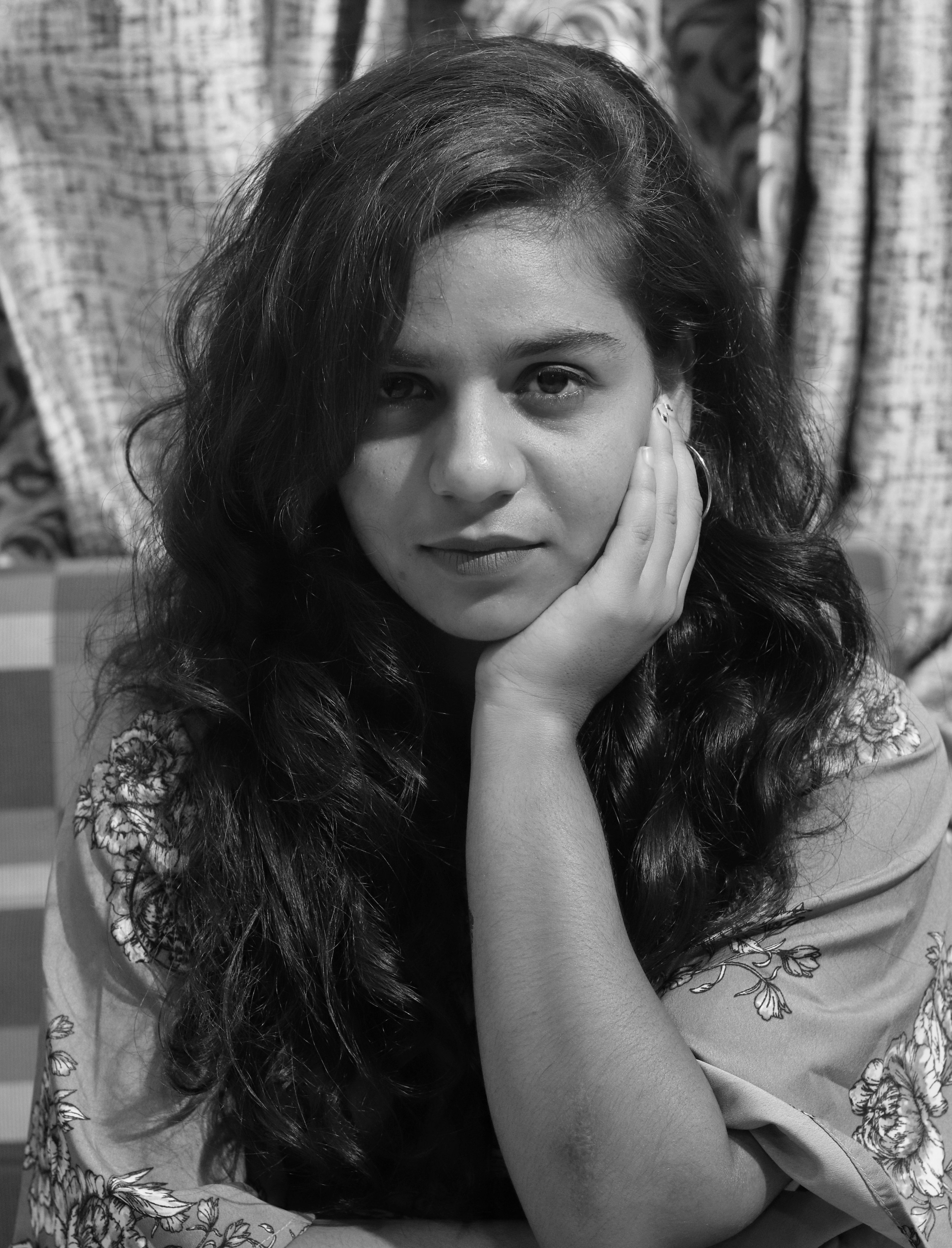 A thoughtful grayscale portrait of a South Asian woman with curly hair, offering an expressive look.