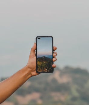 A hand holding a smartphone displaying a scenic mountain view, exemplifying modern technology in nature.