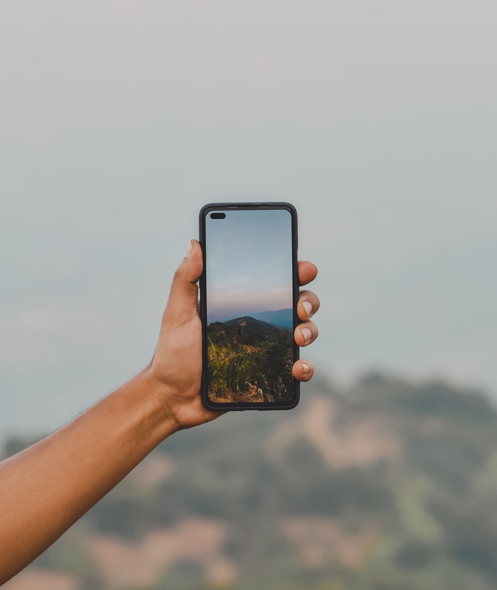 A hand holding a smartphone up against a scenic mountain landscape