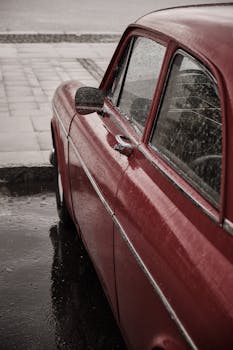 A classic red car parked on a wet street, showcasing timeless elegance and retro design.