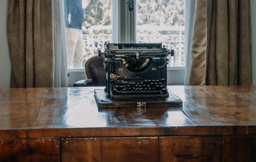 Free A vintage Remington typewriter sits on a wooden desk by a window, evoking nostalgia. Stock Photo