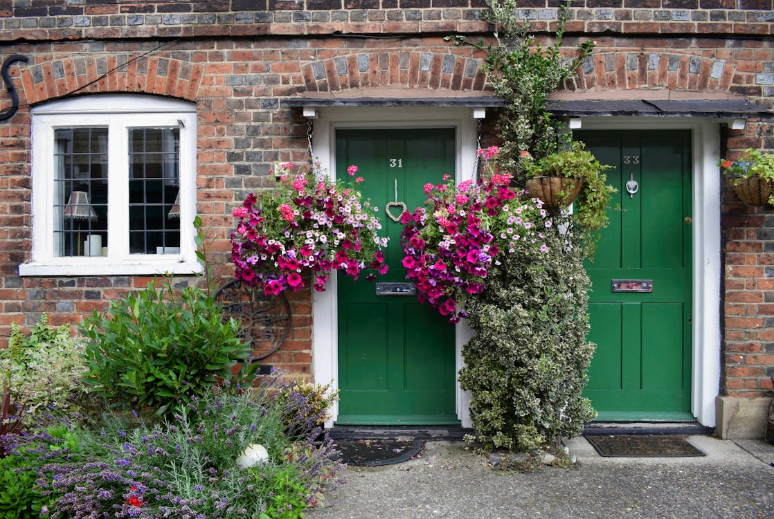 A Green Wooden Doors on a Brick House with Flowers and Plants