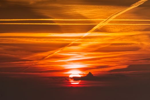 Dramatic sunset with vivid orange and red hues, featuring distinct contrail patterns across the sky.