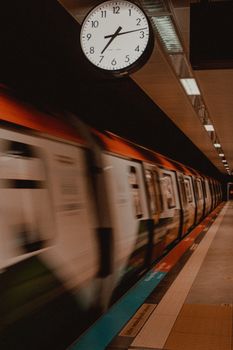 A blurred high-speed train passing through Istanbul station under a clock, captured at night.