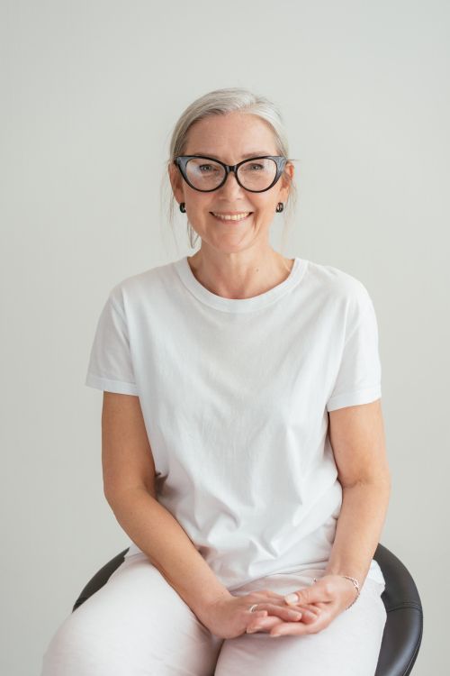 Free Portrait of a happy senior woman wearing eyeglasses and a white shirt while smiling indoors. Stock Photo