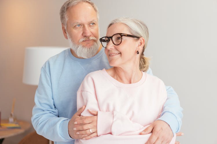 An Elderly Couple Embracing Each Other While Wearing Pink And Blue Sweaters