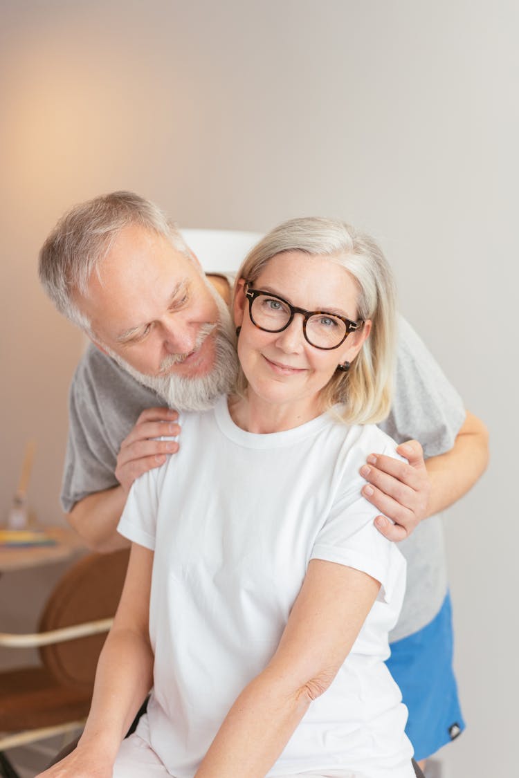 A Bearded Man Embracing A Woman In White Shirt Smiling While Wearing Eyeglasses