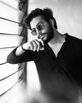 Black and white portrait of a bearded man wearing sunglasses, posing indoors.