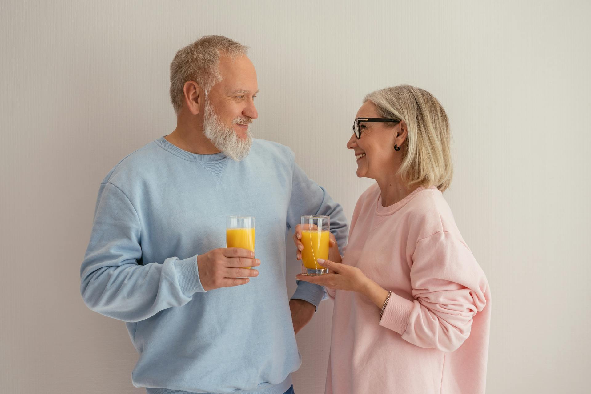 Smiling senior couple holding orange juice glasses in a cozy indoor setting.