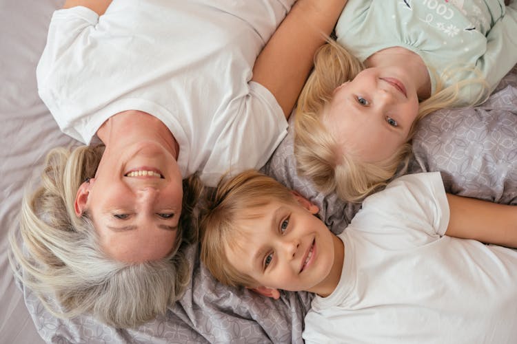 An Elderly Woman Lying On The Bed With Her Grandchildren