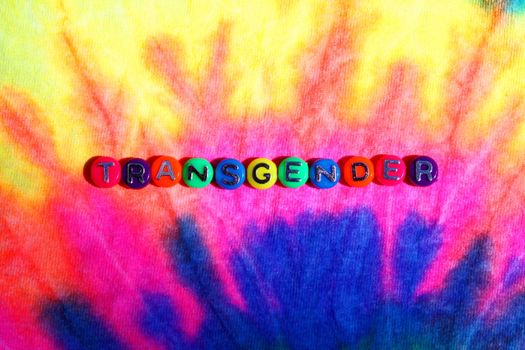 Vibrant close-up of 'TRANSGENDER' text on a colorful tie-dye fabric, symbolizing pride.