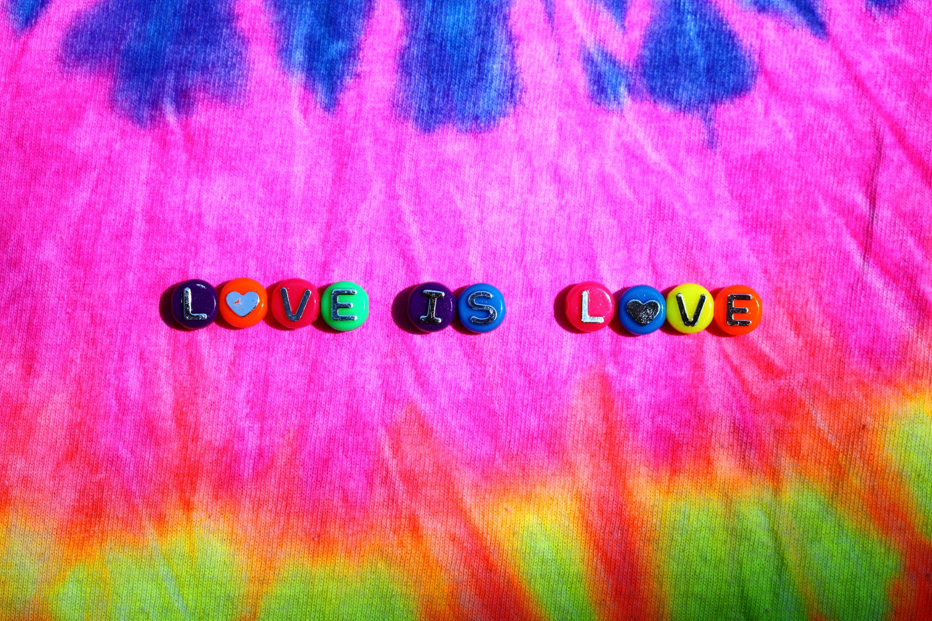 Vibrant tie-dye background with 'Love is Love' text in colorful letters.