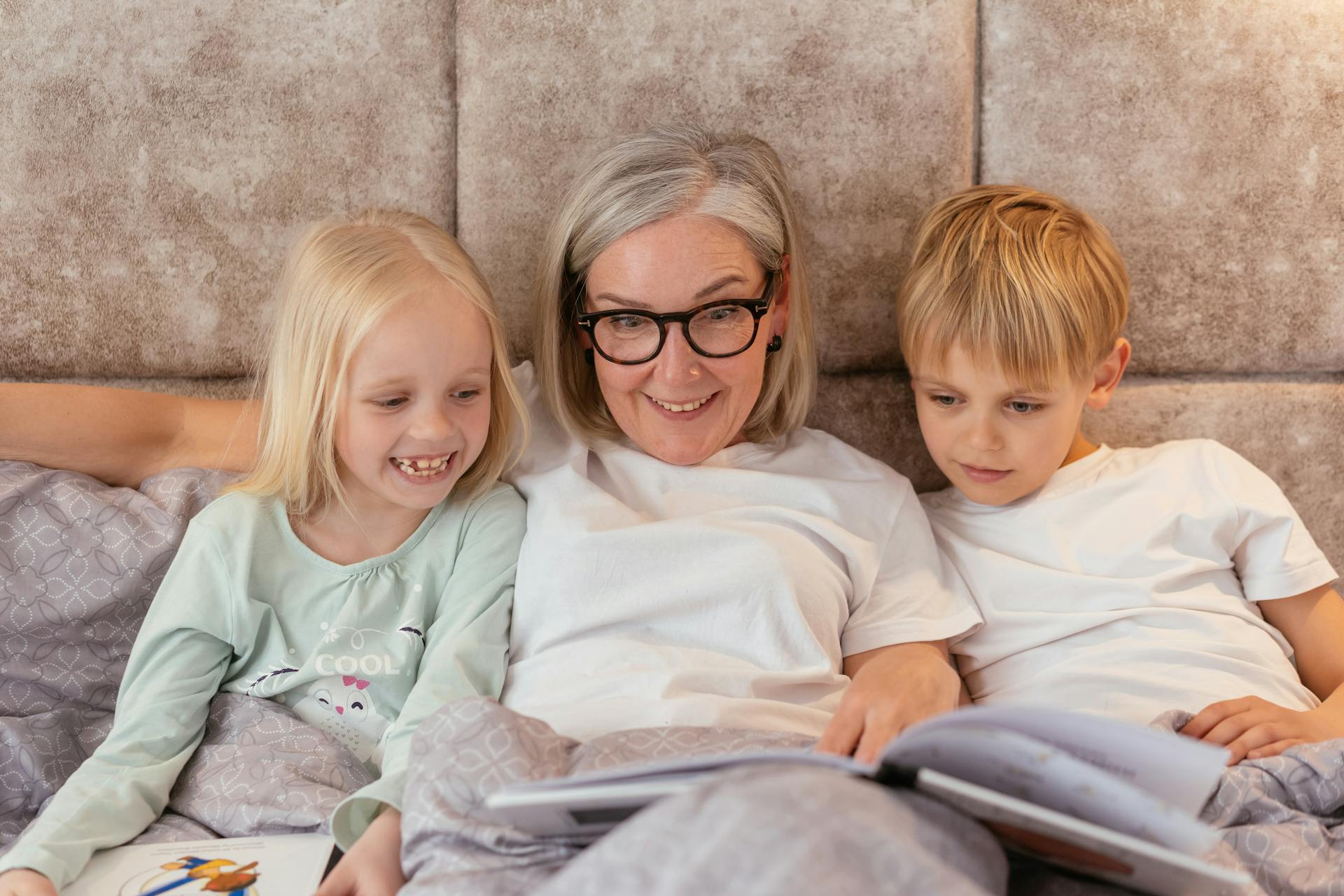 Smiling grandmother reading a book with her grandchildren in bed for family bonding time.