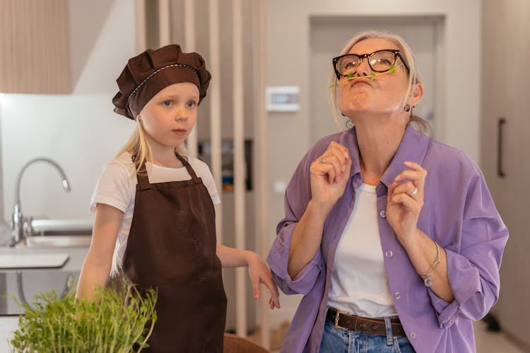 Woman Sniffing A Stem Next To A Girl In An Apron