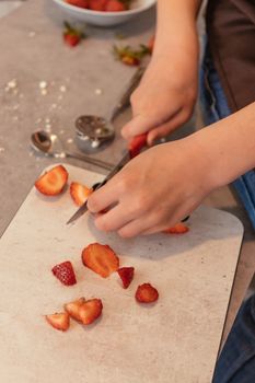 Close-up of hands slicing strawberries on a chopping board, showcasing elegance in kitchen preparation.