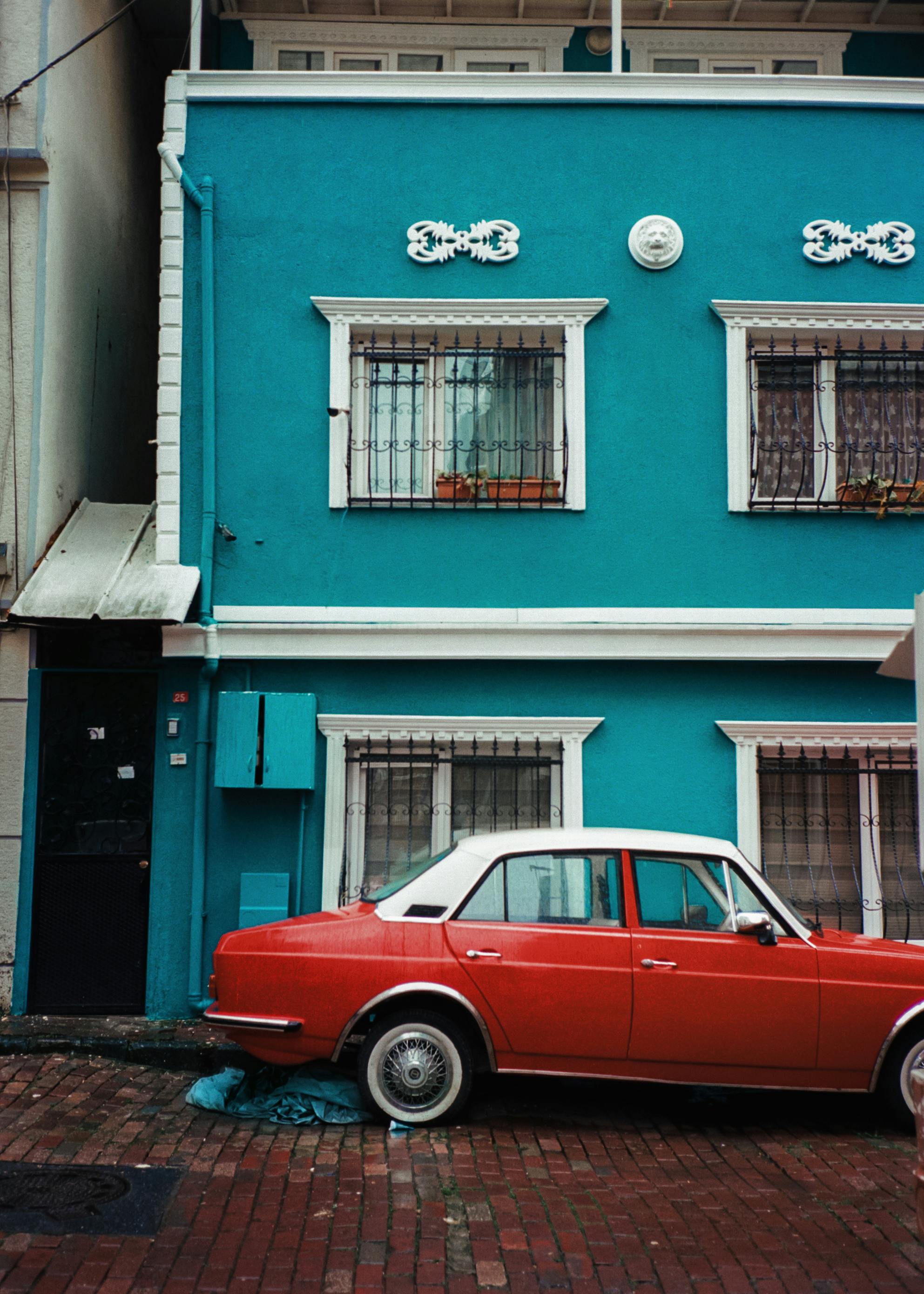 A blue house with a vintage red car parked outside on a cobblestone street in Istanbul.