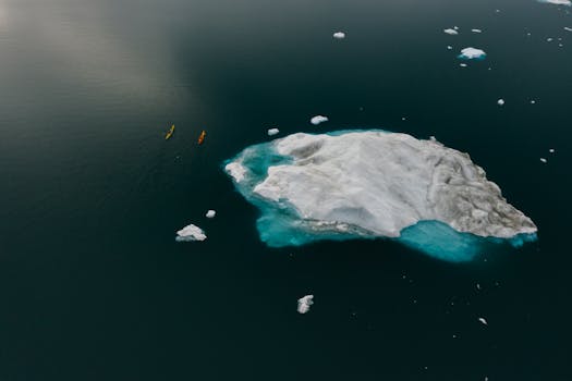 Drone shot capturing colorful canoes navigating near a large iceberg in cold waters. Winter adventure scene.